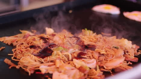 Street-seller-frying-japanese-street-food-Yakisoba-and-pouring-brown-sauce-on-the-teppan