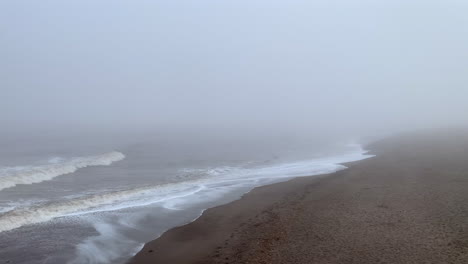 Eine-Neblige-Küste-Mit-Wellen,-Die-Unter-Einem-Nebligen-Grauen-Himmel-Zum-Strandufer-Rollen