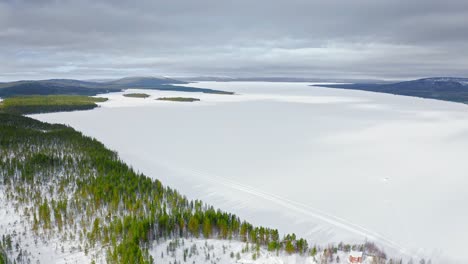 Flight-Above-Evergreen-Woodland-And-Frozen-Spacious-Lake-In-Winter-Season