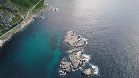 Vista-Panorámica-Desde-Aguas-Azules-Profundas-Con-Isla-Rocosa-Hasta-Vistas-A-La-Montaña-Donde-La-Carretera-Va-Junto-Al-Mar