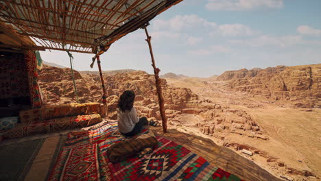 Cinemagraph-seamless-video-loop-of-a-young-female-woman-in-Petra,-Jordan,-sitting-in-a-bedouin-hut-with-colorful-vibrant-carpets-and-a-view-of-the-historic-roman-theater-carved-into-sandstone-rock