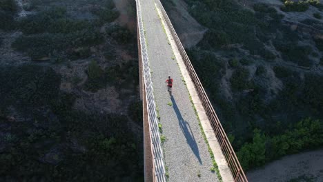 Aerial-drone-view-of-a-biker-crossing-a-huge-old-railway-bridge-in-Via-Verde-Ojos-Negros,-Teruel,-Spain