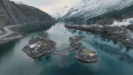 Small-lake-islands-surrounded-by-massive-mountain-range-in-Norway,-loen,-aerial-view