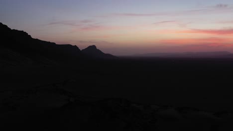 Silhouette-of-mountain-in-desert-at-sunset-with-multicolored-sky,-Morocco