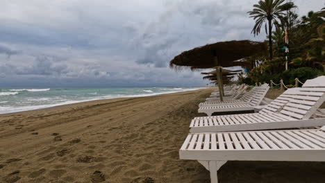 4k-Shot-of-an-empty-beach-with-sunbeds-and-straw-umbrellas-at-Marbella,-Spain
