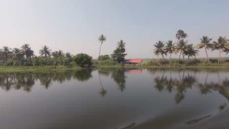 Tropical-landscape,-peaceful-river-surface,-vessel-navigate-along-Kerala-backwaters,-India