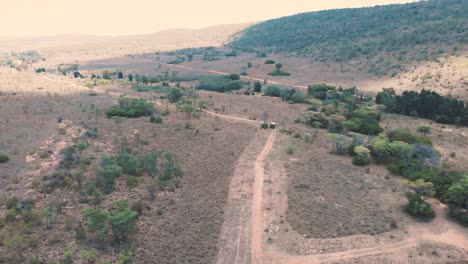 Safari-jeep-on-dirt-road-in-african-savannah-landscape,-drone-shot