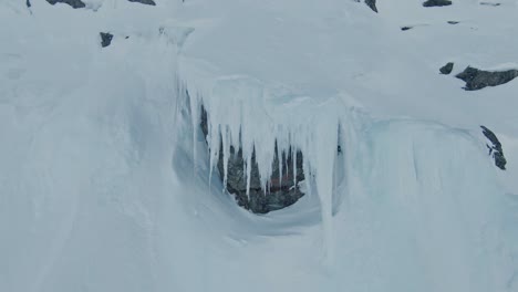 Massive-icicle-hanging-on-mountain-slope-side-in-Norway,-aerial-view