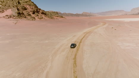 Aerial-Follow-A-Car-Driving-In-Sweeping-Sand-Desert-In-Wadi-Rum,-Jordan