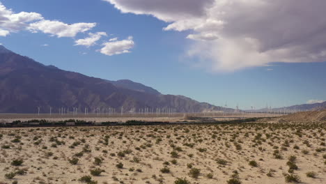Drone-flies-close-to-ground-towards-train-passing-by-in-front-of-windmill-farm-in-Palm-Springs