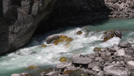 The-blue-gray-glacial-water-in-the-river-at-the-base-of-a-huge-rock