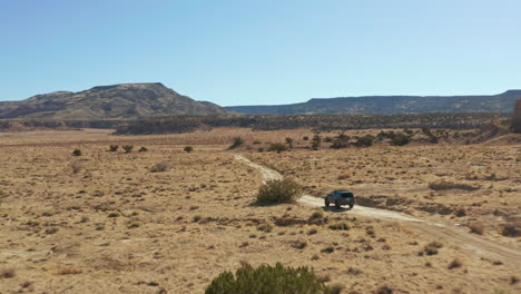 Fast-moving-aerial-following-car-down-remote-dirt-road-in-open-desert