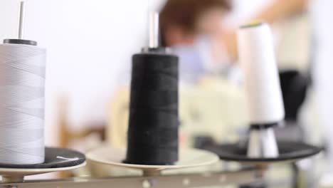 Panning-shot-of-thread's-spools-on-a-sewing-machine-with-a-latin-seamstress-working-in-the-background