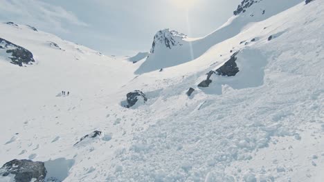 Avalanche-debris-on-pure-white-mountain-slope-on-sunny-day,-aerial-ascend-view