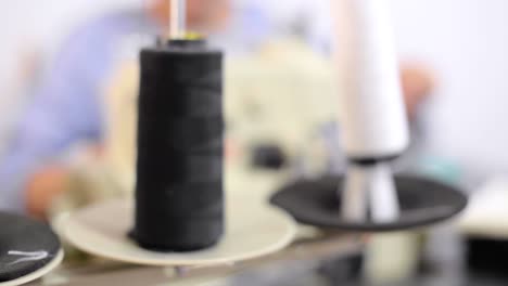 Panning-shot-of-thread's-spools-on-a-sewing-machine-with-a-seamstress-working-in-the-background