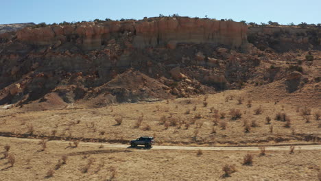 Aerial-following-car-on-desert-road-with-large-rock-formation-in-background