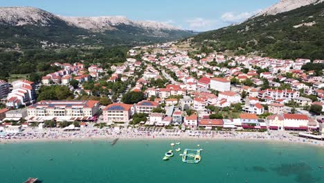 Baska-Beach,-Krk-island,-Croatia---Aerial-Drone-View-of-the-Seaside-Resort-with-Coastline,-Tourists,-Boulevard,-Sunbeds-and-Water-Playground