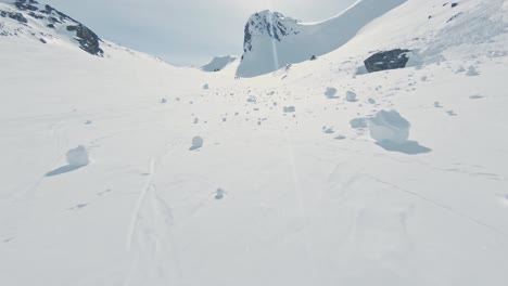 Three-friends-climbing-up-snow-covered-mountain-for-skiing-in-Norway,-aerial-FPV-view