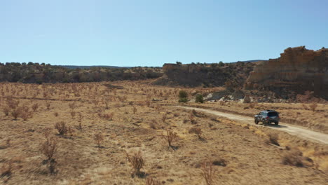 Aerial-following-car-through-desert-landscape-on-remote-dirt-road,-4K