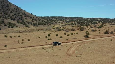Aerial-following-vehicle-through-desert-landscape-on-remote-dirt-road