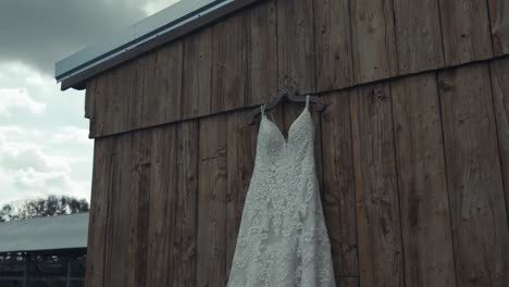 Schwenk-Eines-Wunderschönen-Hochzeitskleides,-Das-An-Der-Wand-Eines-Holzschuppens-Hängt