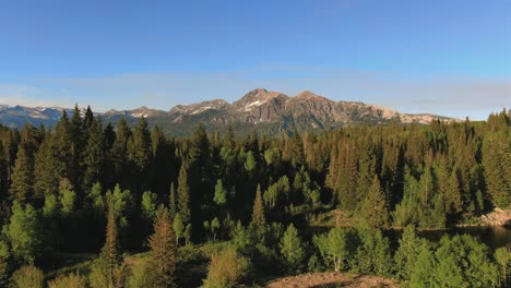 Drone-Flying-Over-Lake-And-Pine-Trees-To-Reveal-Beautiful-Mountain-Peak-Surrounded-By-Woods