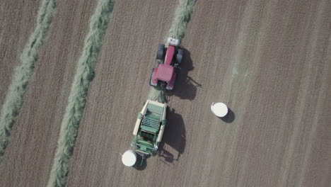 Industrial-equipment-packing-haybales-into-white-plastic,-aerial-top-down-view