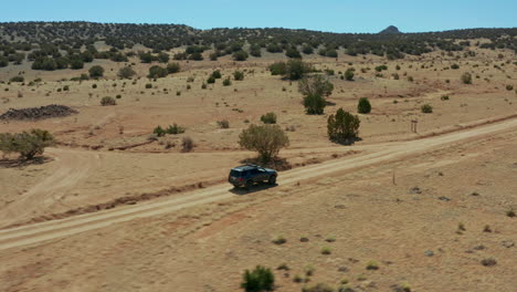 Aerial-panning-up-to-follow-4x4-SUV-on-dirt-road-in-desert-landscape