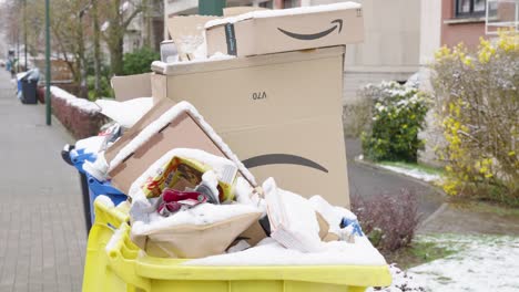 Überquellende-Mülleimer,-Die-Bei-Schneefall-Mit-Amazon-Paketen-In-Der-Stadtstraße-Bedeckt-Sind