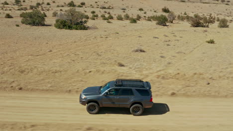 Close-aerial-tracking-SUV-driving-on-dirt-road-through-open-desert-terrain