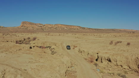 Aerial-as-car-drives-through-desert-ravine-on-rugged-dirt-road-in-New-Mexico