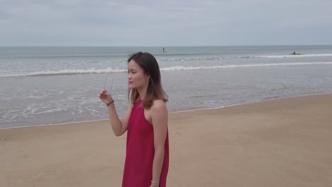 Junge-Asiatische-Frau-Trägt-Rotes-Kleid-Und-Geht-Entspannt-Am-Strand-In-Den-Sommerferien-In-Slowmotion