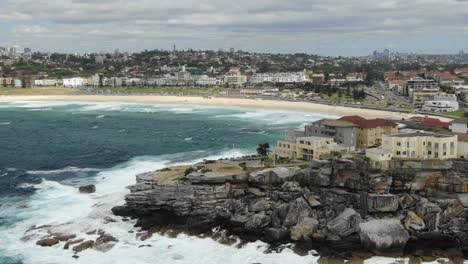Jagged-coastline-with-Sidney-skyline-and-Bondi-bay-beach-and-stormy-waves-crashing-on-cliff-in-Australia