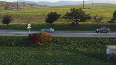 Two-cars-travelling-along-a-rural,-country-road-through-the-vast,-open-landscapes-of-Slovakia,-Europe