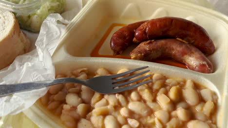 Takeaway-food-in-styrofoam-packaging---white-beans-and-sausages-with-shredded-cabbage-salad,-top-view-handheld-footag