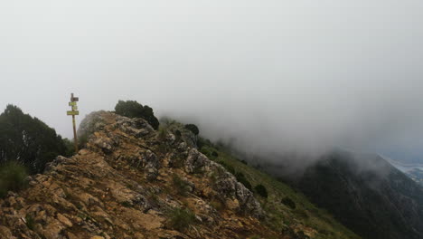 Toma-Estática-De-4k-De-Niebla-Y-Nubes-Alrededor-De-Una-Cresta-De-Montaña-Con-Un-Cartel-De-Senderismo