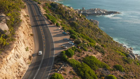 Vehicles-Driving-Along-Victoria-Road-With-Ocean-Views-Near-Oudekraal,-South-Africa