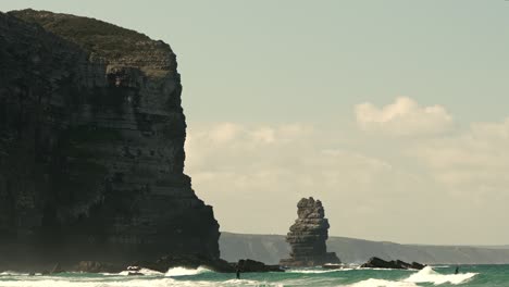 People-paddle-boarding-on-low-waves-next-to-a-tall-cliff-on-a-sunny-day