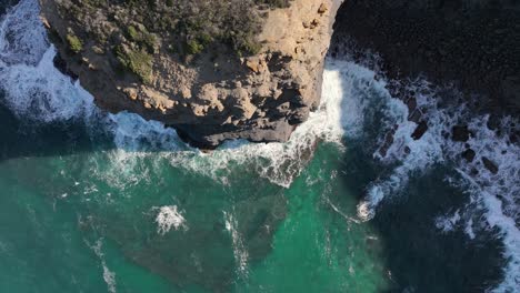 Aerial-shot-flying-horizontally-over-a-sunlit-cliff-and-turquoise-water