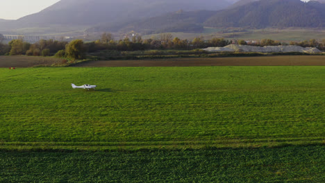 Un-Pequeño-Avión-Blanco-Despegando-De-Un-Campo-De-Hierba-Con-Montañas-Como-Telón-De-Fondo-En-Eslovaquia