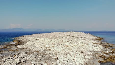 Der-Felsige-Strand-Von-Paralia-Emplisi-Trifft-Auf-Das-Klare-Blaue-Wasser-Des-Weiten-Ozeans-In-Griechenland---Luftaufnahme-Nach-Vorne