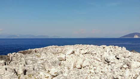 Weiße-Steinige-Oberfläche-Von-Paralia-Emplisi-Beach,-Kefalonia-In-Griechenland-Mit-Blick-Auf-Das-Endlose-Blaue-Ozeanwasser---Vorwärts-Antenne