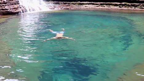 Junger-Mann,-Der-Im-Blauen-Klaren-Wasser-Des-Wasserfalls-Von-Oben-Schwimmt