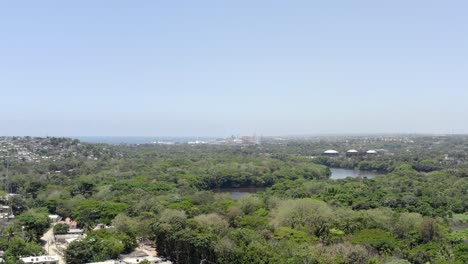 Aerial-forward-over-green-area-of-Santo-Domingo-Oeste-with-river-in-background