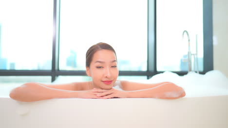 Close-up-of-an-attractive-woman-in-a-bubble-bath-with-her-arms-and-chin-resting-on-the-edge-of-the-tub