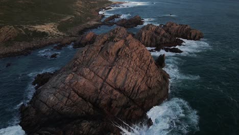 A-dynamic-aerial-footage-of-large-offshore-boulders-with-strong-waves-around-it-in-the-golden-hour