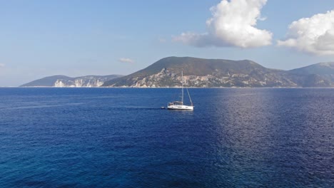 Boat-Sailing-Through-The-Blue-Ocean-On-A-Cloudy-Day-Overlooking-The-Mountainside-Of-Paralia-Emplisi-Kefalonia,-Greece--Lateral-Aerial-Shot