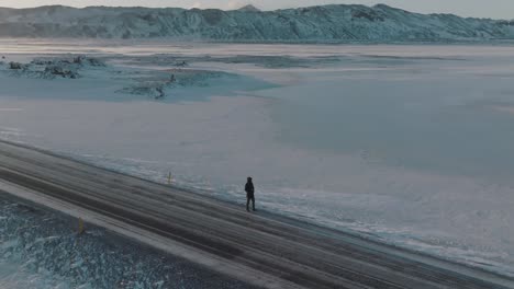 Trekker-on-Lonely,-Icy-Road-in-Snowy-Winter-Iceland-Landscape---Aerial