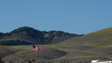 The-US-flag,-stars-and-stripes,-old-glory-flying-in-front-of-rolling-hills-and-a-blue-sky