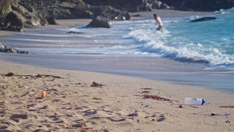 Meerblick-Auf-Den-Sandstrand-Von-Cornwall-Mit-Weggeworfenen-Plastikflaschen-Und-Einem-Mann,-Der-Im-Hintergrund-Schwimmt---Statisch